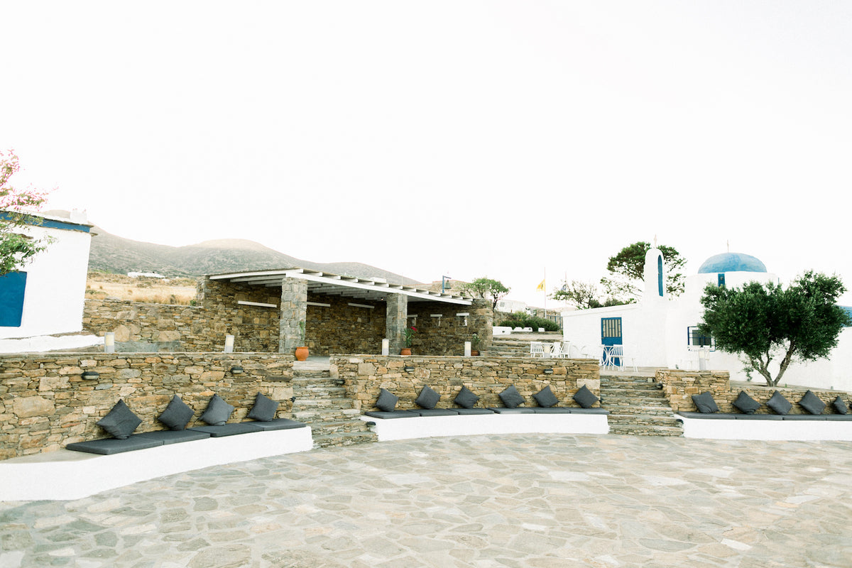 Stone terrace with grey cushions and sofas, with the view to the Aegean sea, at The Secret View, a wedding venue with a sea view in Paros, Greece