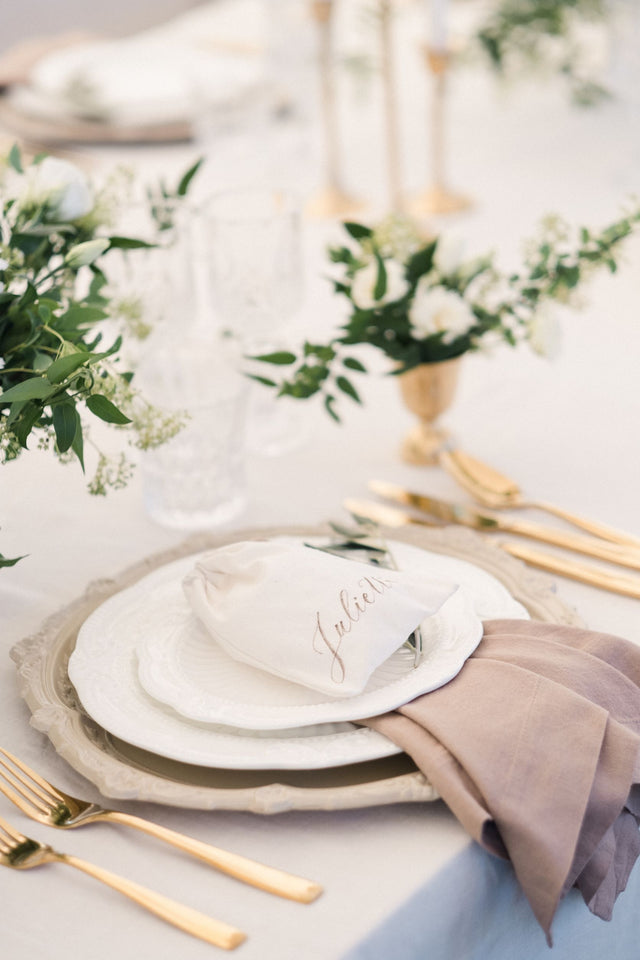 Table decoration with taupe napkin and gold cutlery, linen bag in lieu of a placecard. A natural, authentic, outdoor wedding decoration in Paros, Greece.